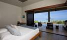 A bright bedroom features a king bed and expansive glass doors that open to a private terrace, offering direct ocean views and abundant natural light.