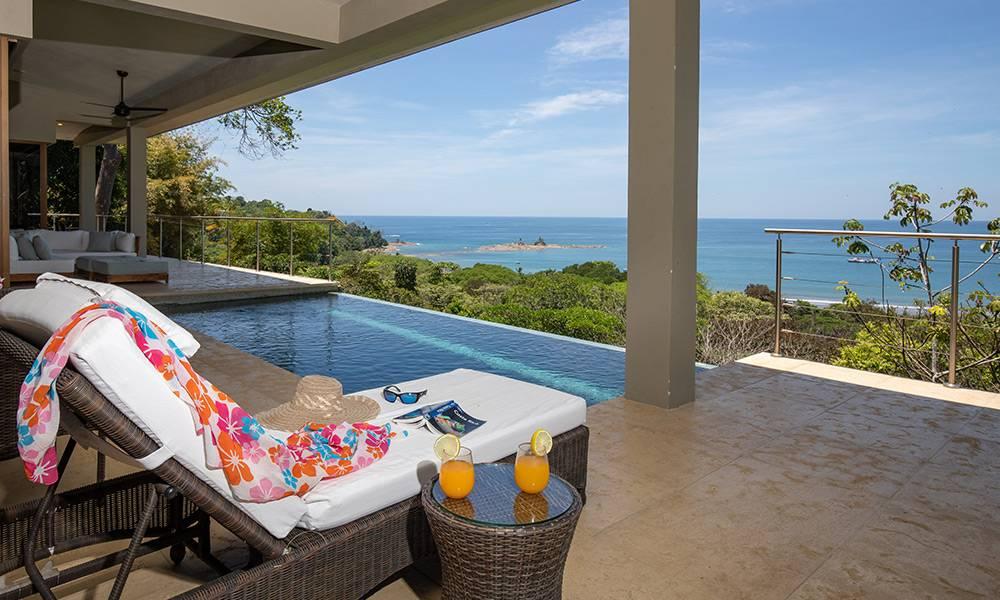 The infinity-edge saltwater pool and covered terrace provide direct, expansive views of the Pacific Ocean and lush coastline, bathed in natural light.