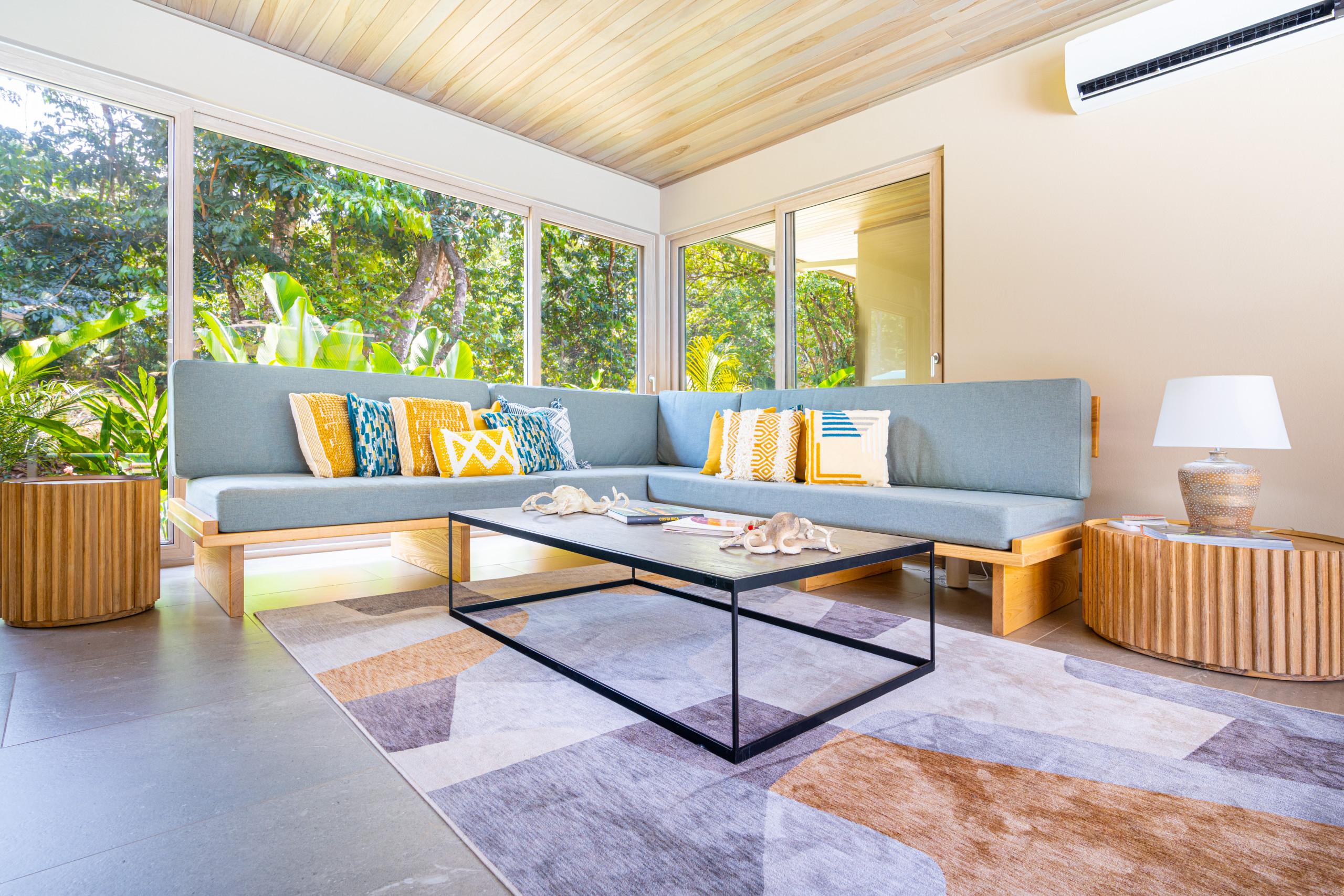 This living room offers a spacious sectional sofa, a warm wooden ceiling, and expansive windows that immerse guests in the surrounding jungle views.