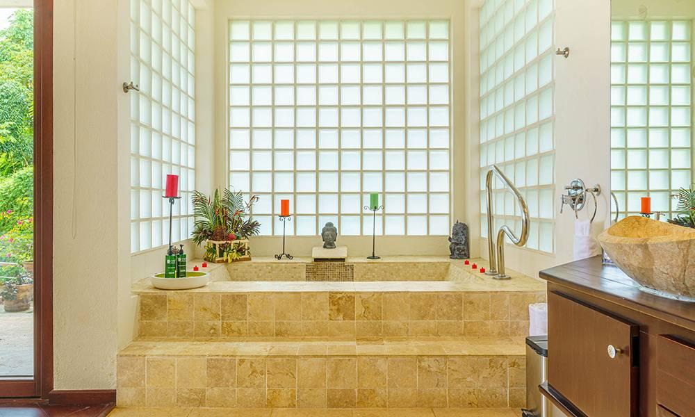 This master bathroom showcases a spa-sized coralline-tiled bathtub, naturally lit by surrounding glass block walls, and connected to lush outdoor greenery through a glass door.