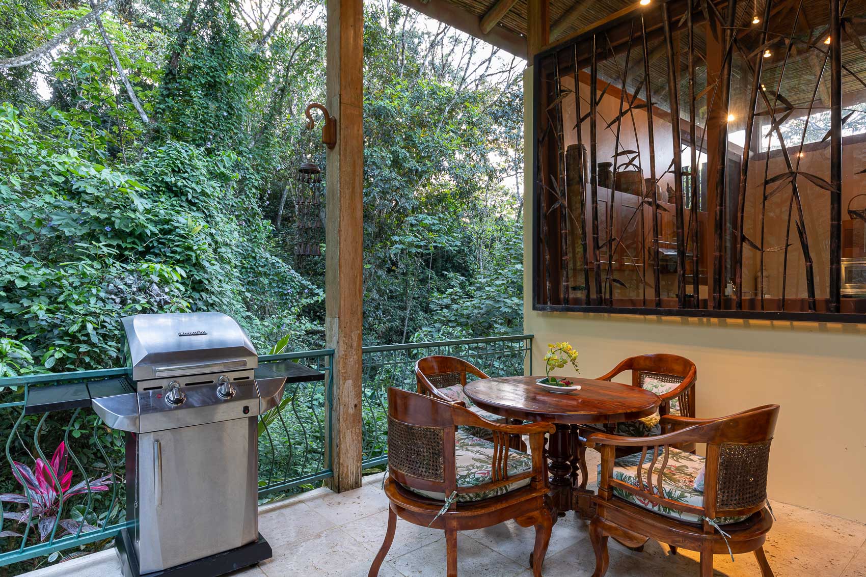 A Balinese-inspired outdoor terrace with a tiled floor and bamboo roof features a dining table and grill, offering views directly into the dense tropical jungle canopy.