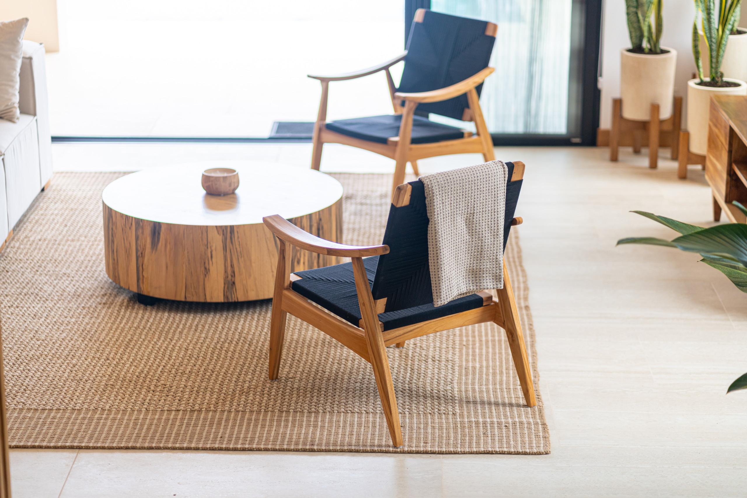 This bright living space features modern wooden chairs and a natural wood coffee table on a woven rug, bathed in natural light from large sliding glass doors.