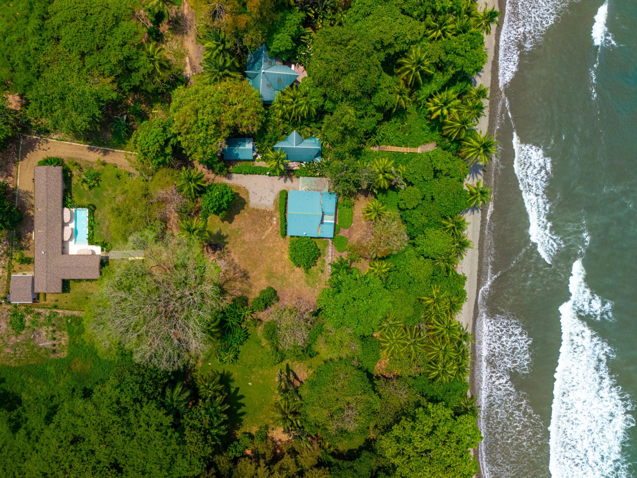 An aerial view reveals the property's buildings and private pool framed by dense tropical jungle, leading directly to a sandy beach and the Pacific Ocean.