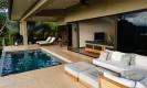 An expansive, sunlit terrace features a saltwater pool and a shaded lounge area, opening through sliding glass doors to interior living spaces framed by lush tropical views.
