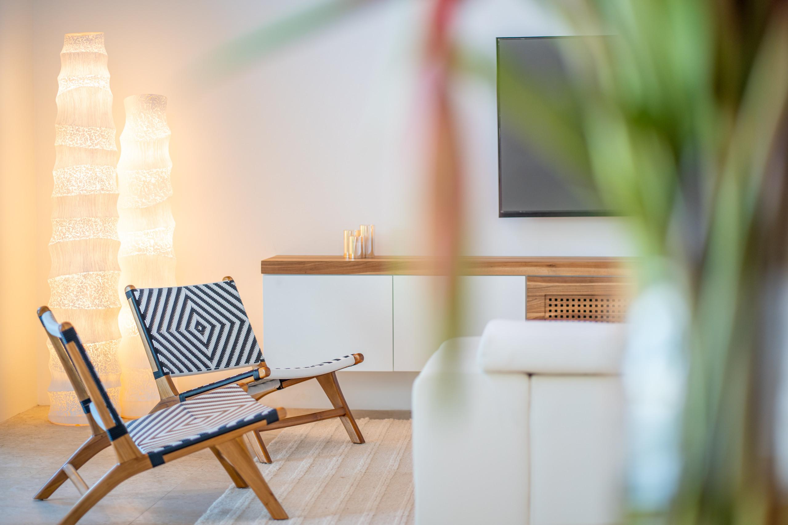 A contemporary living space features modern woven chairs, a wall-mounted media console with a television, and soft ambient floor lighting.