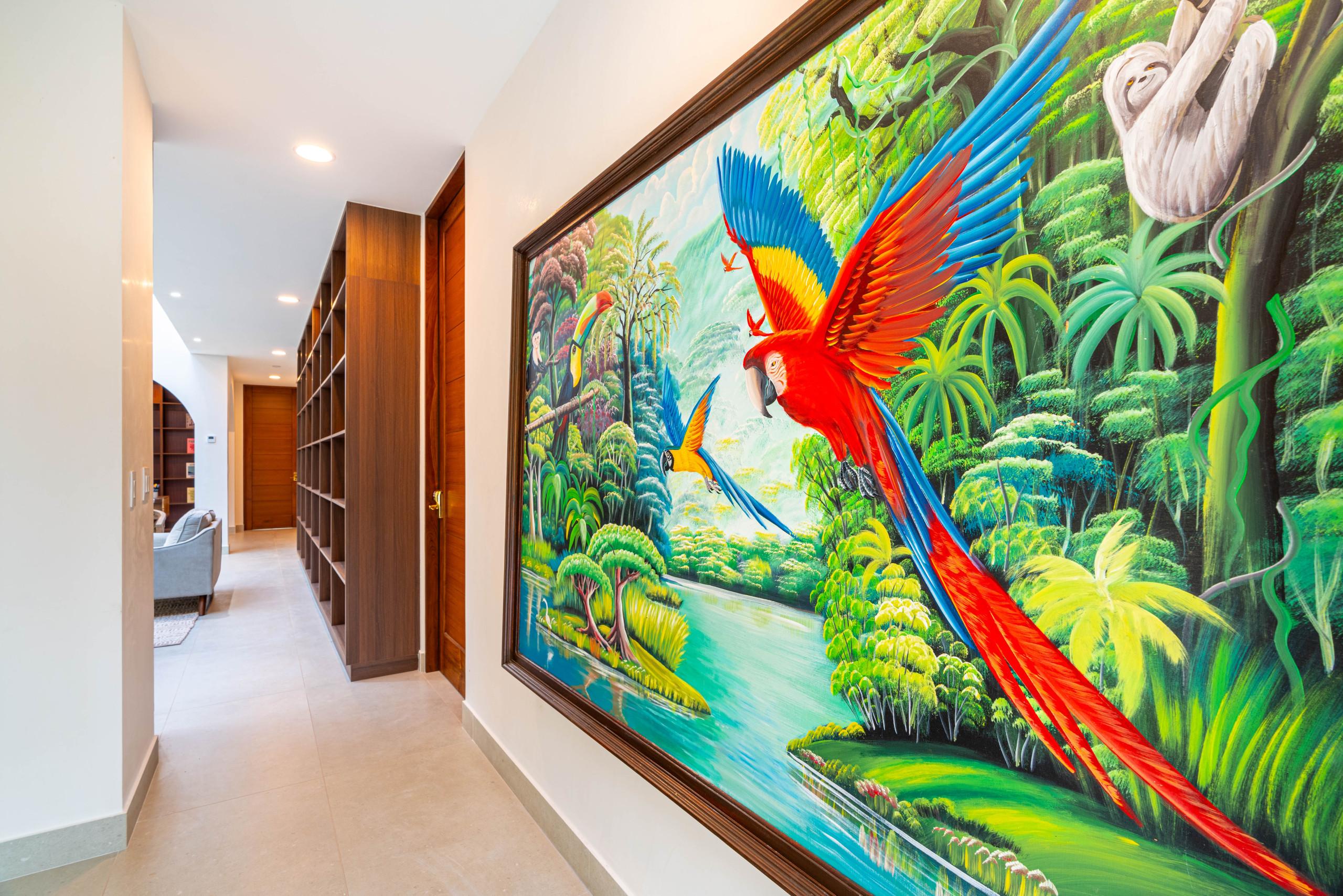 A bright library hallway features extensive dark wood shelving, recessed lighting, and a large, colorful mural depicting a vibrant tropical rainforest scene.