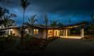 The modern villa entrance, defined by a distinctive roofline and warm interior lights, creates a welcoming ambiance under the night sky.