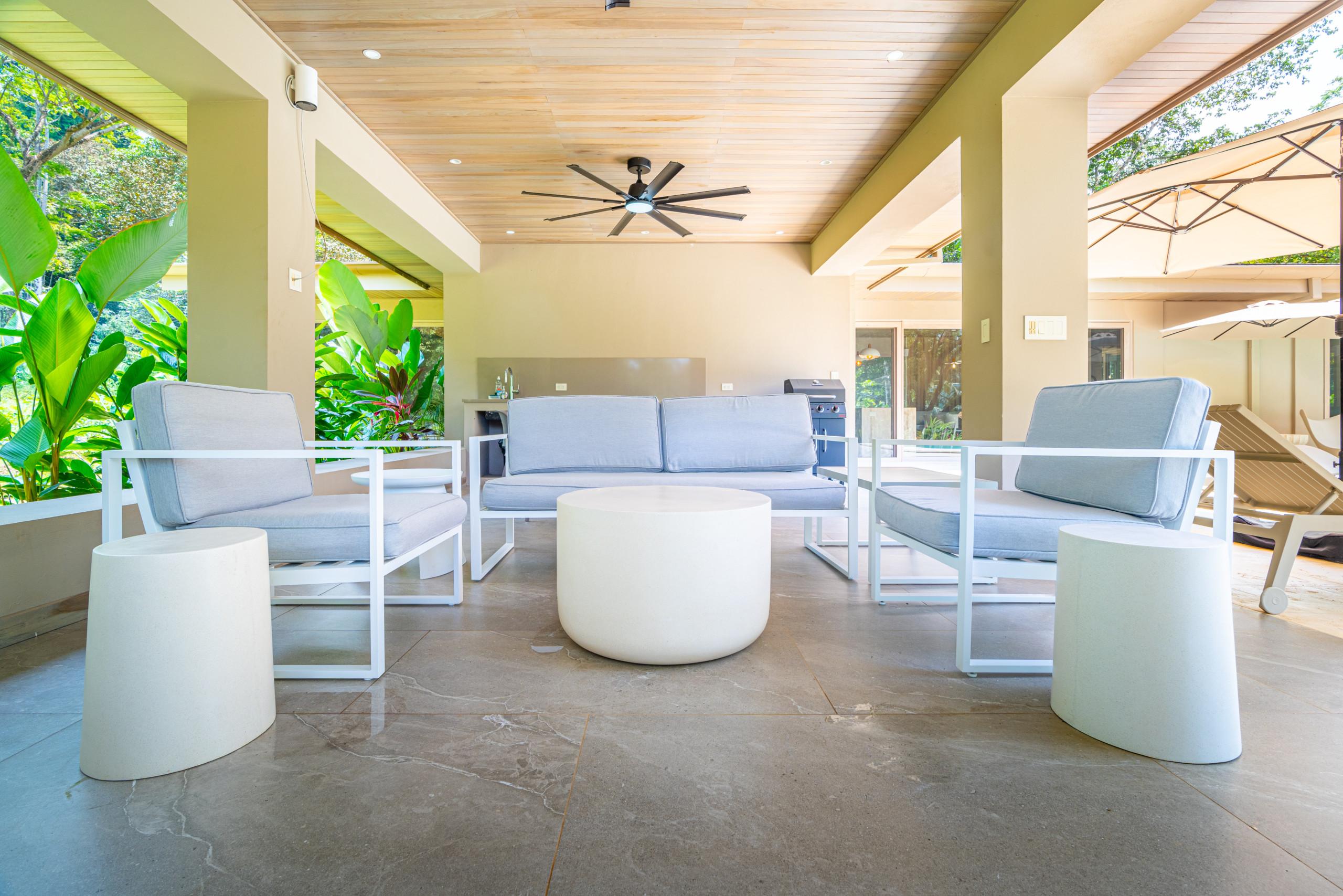 A spacious covered terrace features contemporary outdoor seating, a wet bar, and a grill, with open views of the lush tropical garden and ample natural light.