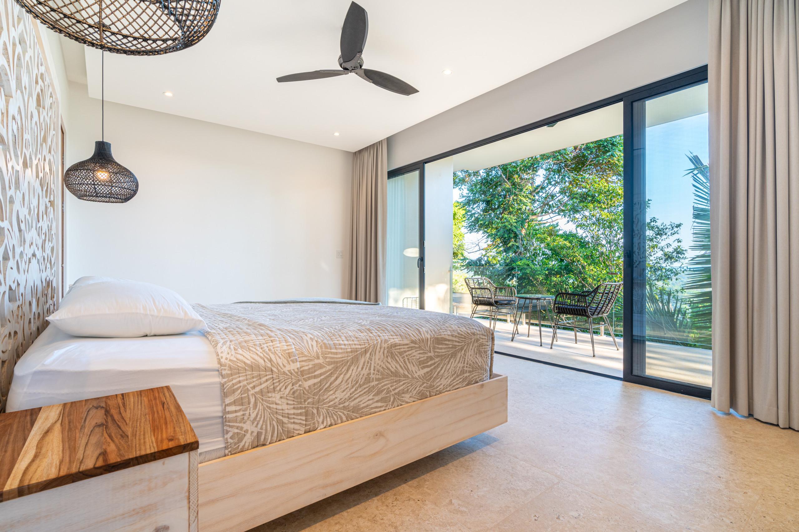 This king bedroom features a carved headboard and glass sliding doors that open to a private terrace overlooking the tropical canopy.
