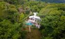The multi-level villa, featuring an infinity pool and glass-walled living spaces, is set into a lush hillside surrounded by dense jungle.