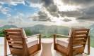Two natural wood lounge chairs face an expansive vista of verdant jungle and distant mountains from an open terrace.
