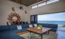 This living space features a high ceiling, a large sectional sofa, and a wall that opens completely to the ocean, allowing for abundant natural light and sea breezes.