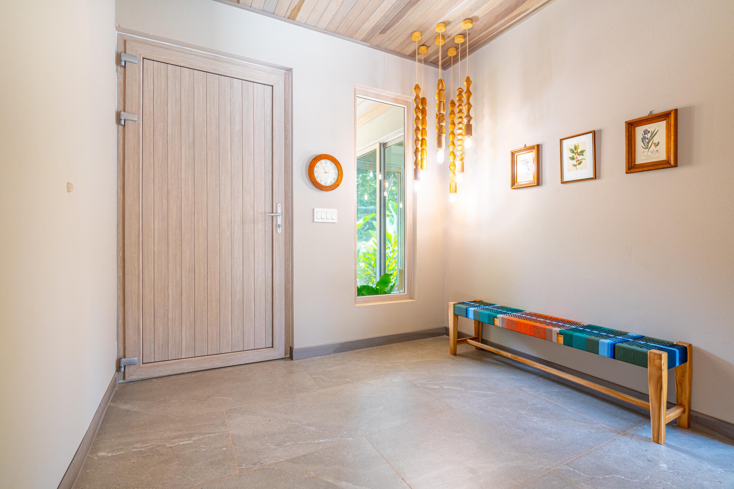 The bright entryway features a natural wood plank ceiling, a large wooden door, and a window with views of the lush tropical garden.