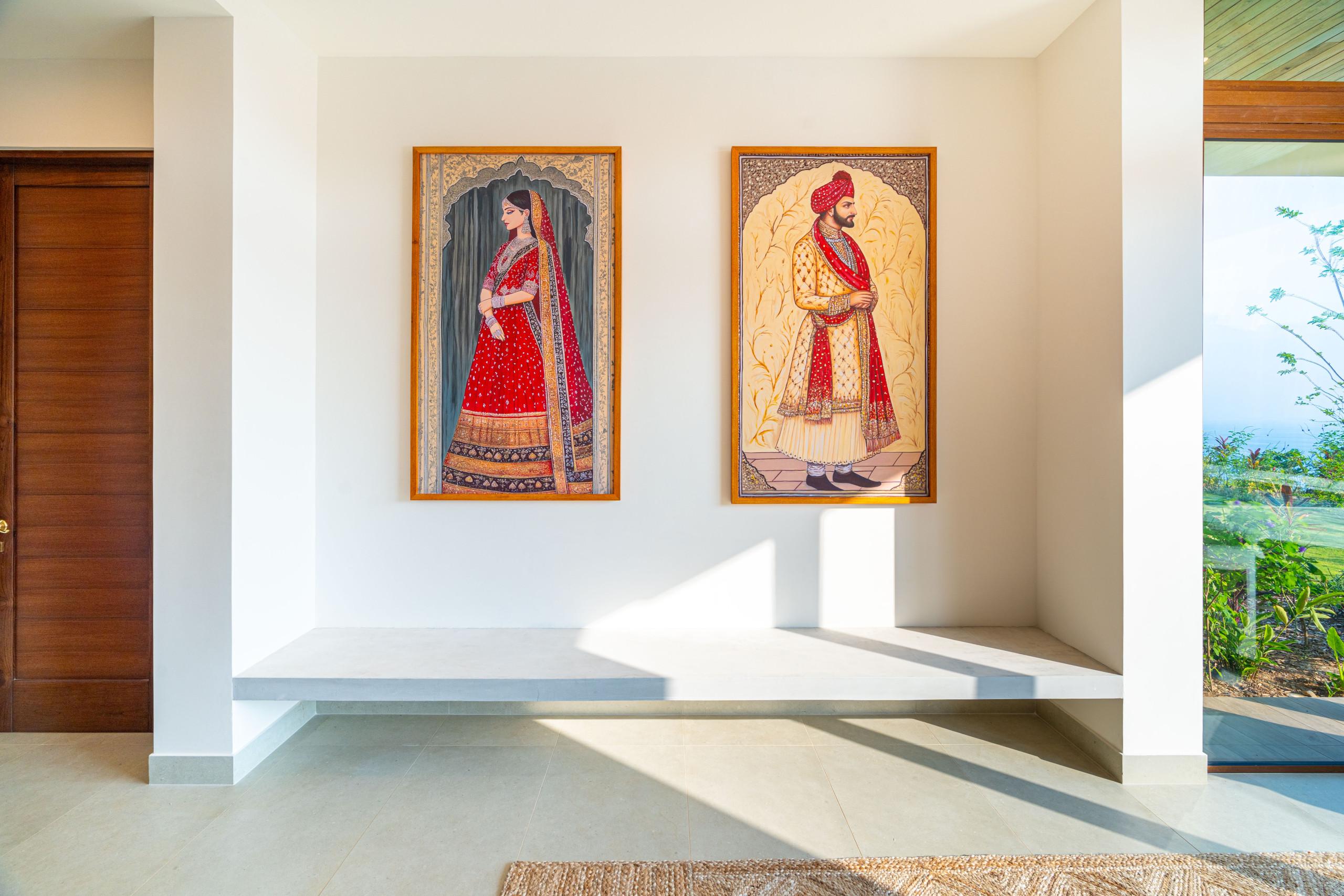 A bright hall, featuring Balinese-inspired artwork and a low bench, opens to tropical greenery and distant ocean views through a large glass panel, complemented by a warm wood door.