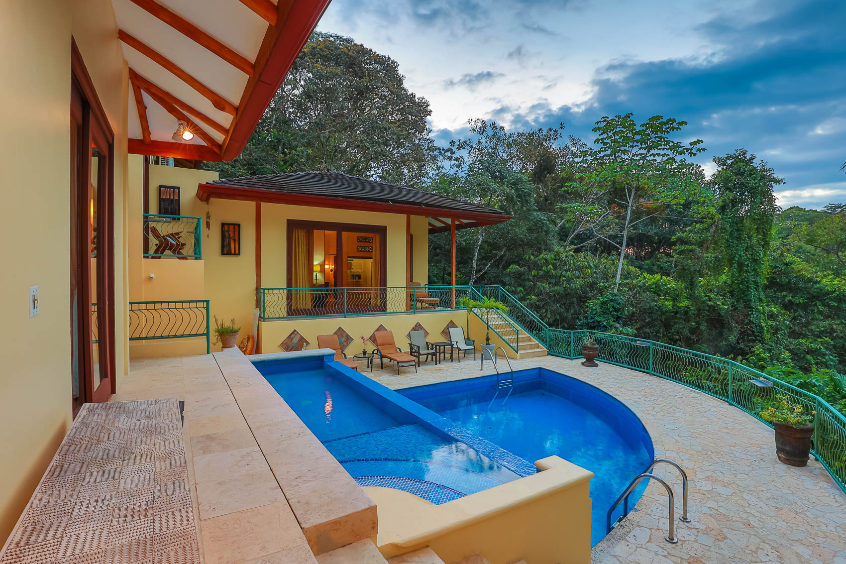The Balinese-inspired villa features two distinct pools, a stone patio, and a covered terrace offering expansive views of the surrounding tropical jungle under a soft, natural light.